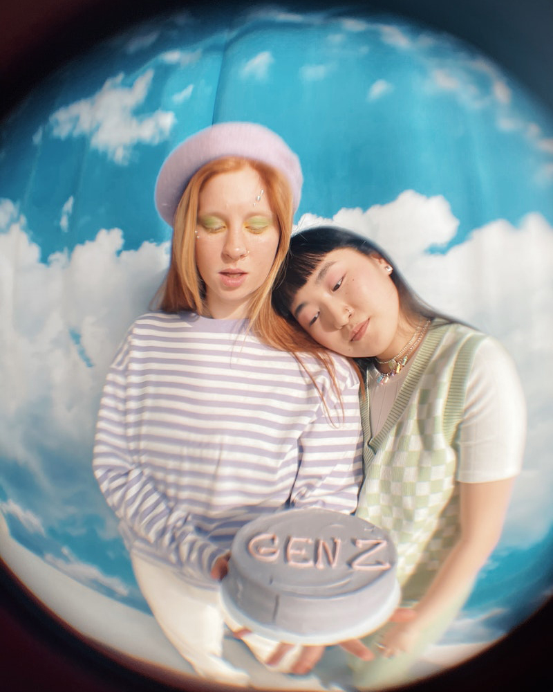 Aesthetic image of two young Generation Z women holding a cake on a sky background