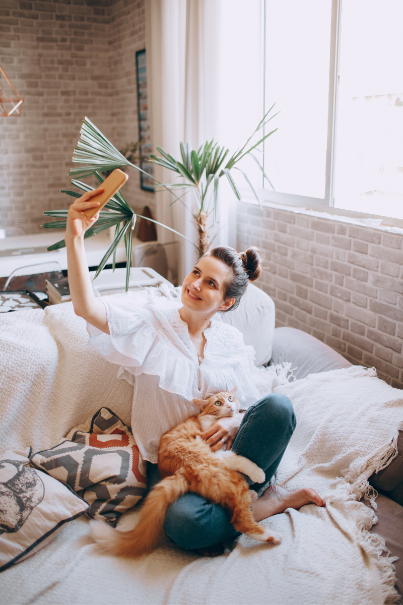 Woman sits with cat on couch to take a selfie