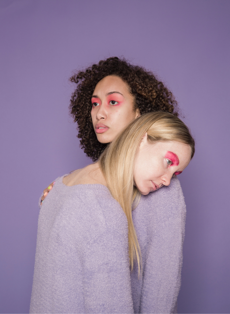 Two women wearing light purple sweaters on a violet background